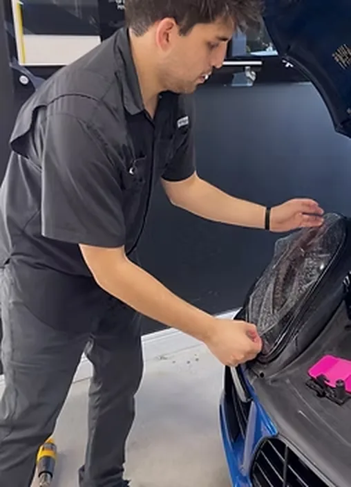An installer working film across the front end of a car