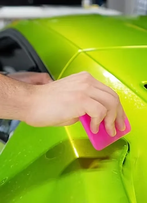 A squeegee flattening film across a green supercar panel